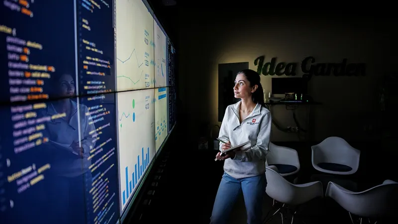 Female in an Indiana University sweatshirt reviews code and analytics on a media display.