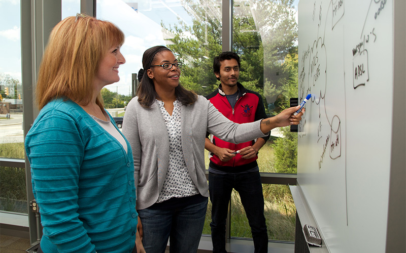 People stand at an I-Light whiteboard, discussing something written on it.